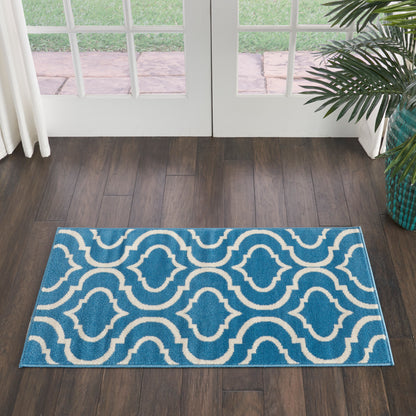 Blue rug with white interlocking wave pattern on dark wood floor in front of glass double doors; teal plant pot nearby.