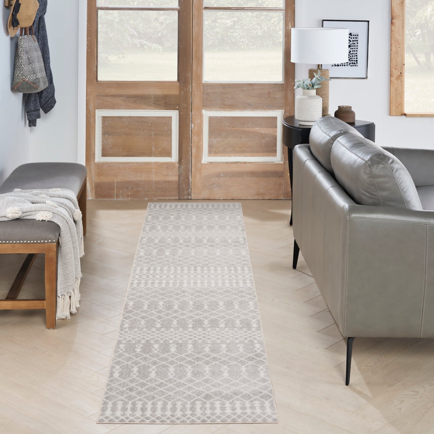 Long grey patterned woven runner rug on light wood floor, between a grey sofa and bench in a modern living room.