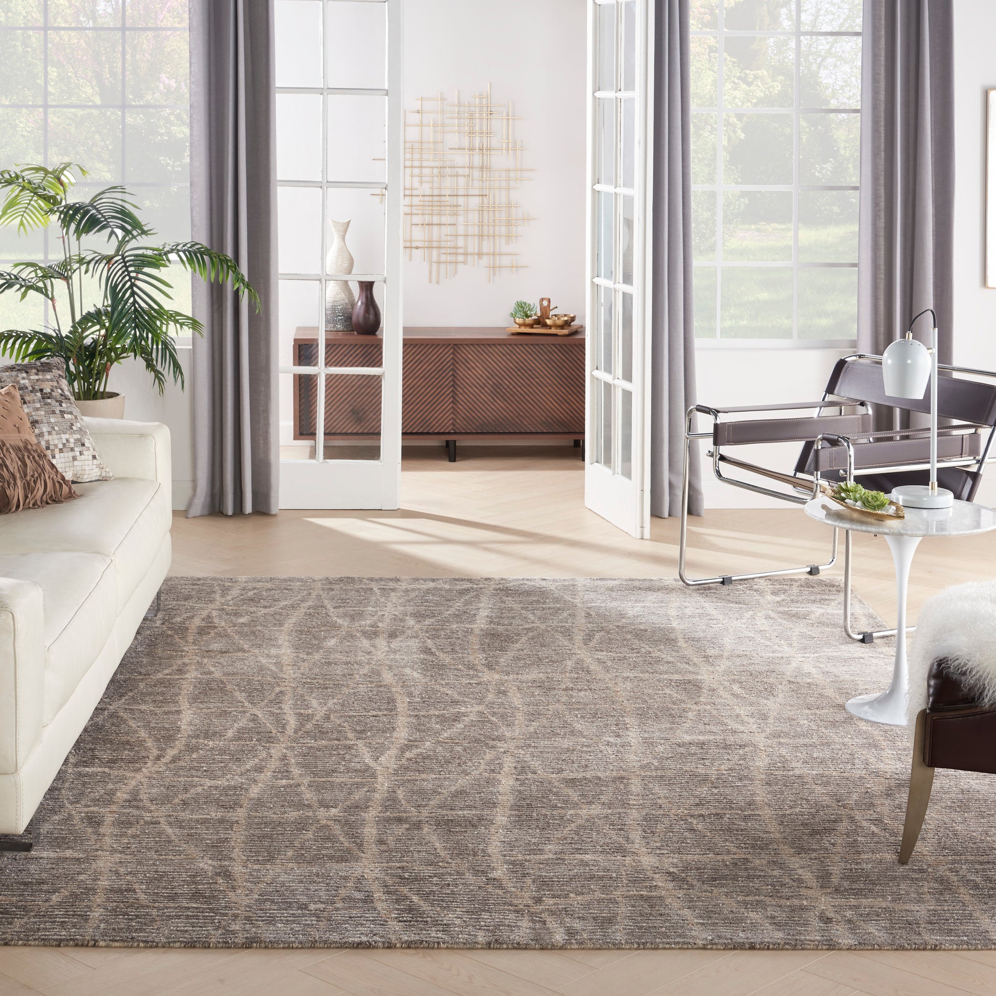 Large gray area rug with soft looping pattern in a bright modern living room; beige sofa, glass doors, metal lounge chair.