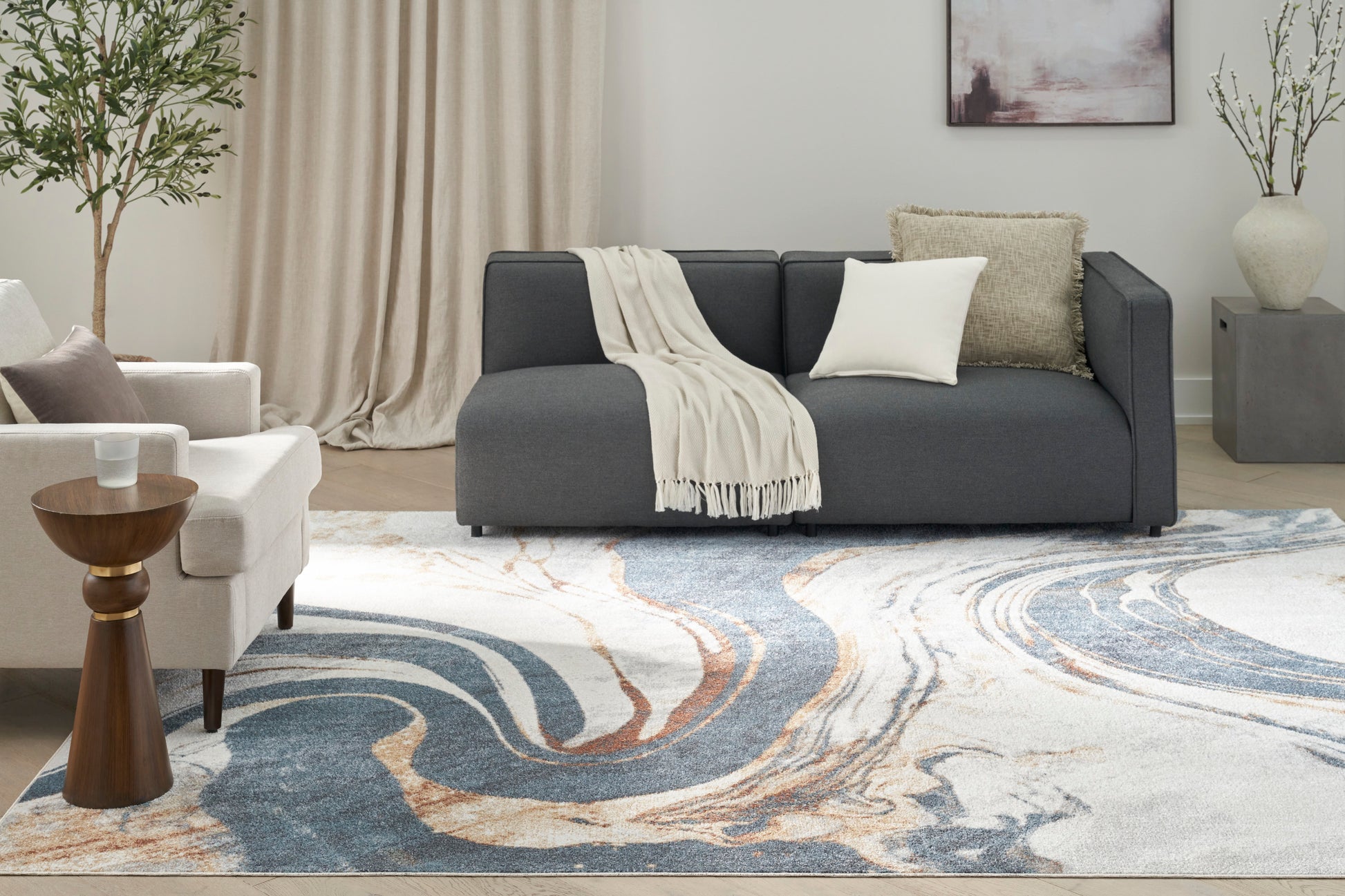 Coastal living room with dark gray sofa, cream throw, white cushion, and a blue swirled rug.