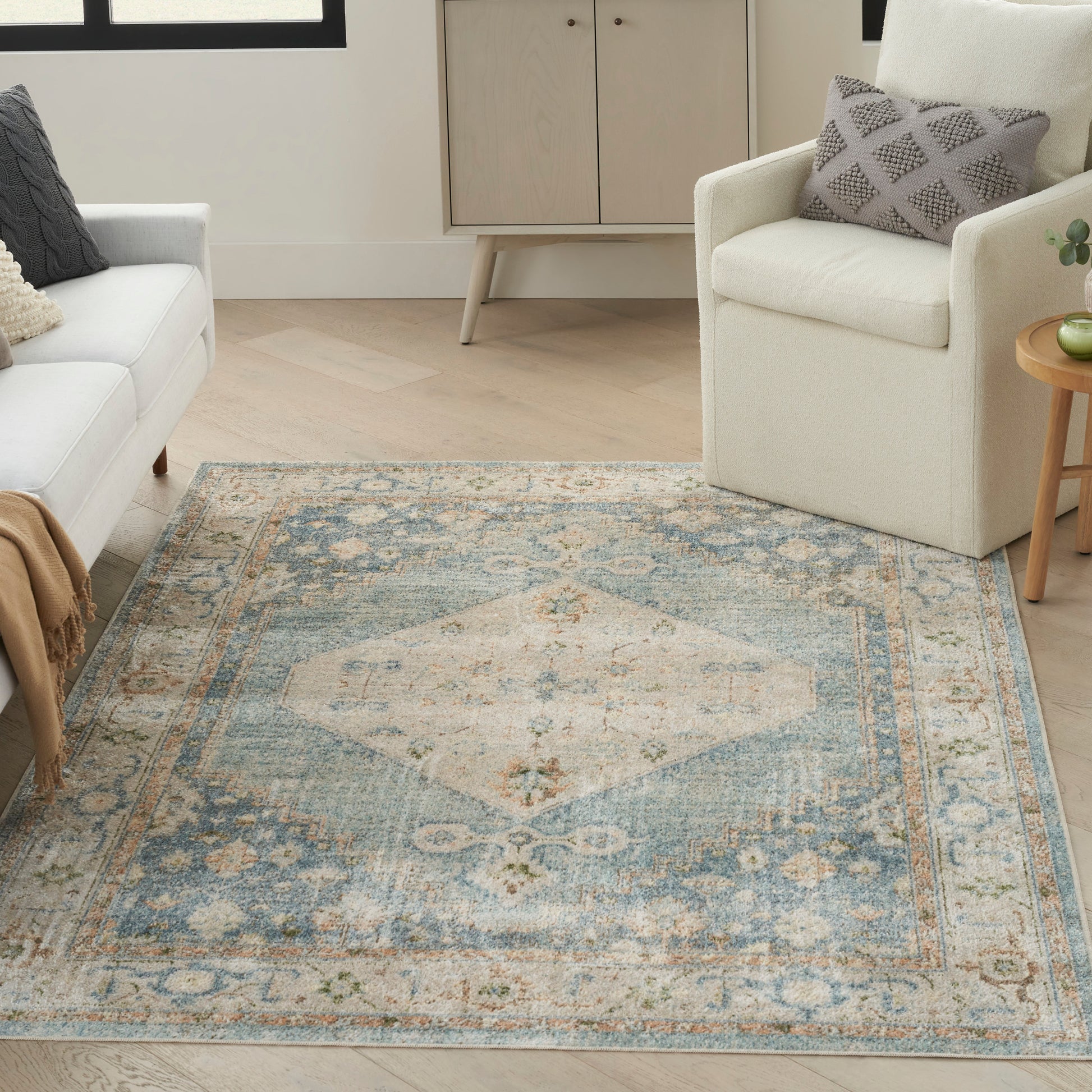 Blue oriental area rug with ivory central diamond medallion & ornate border in a light living room with cream sofa & armchair