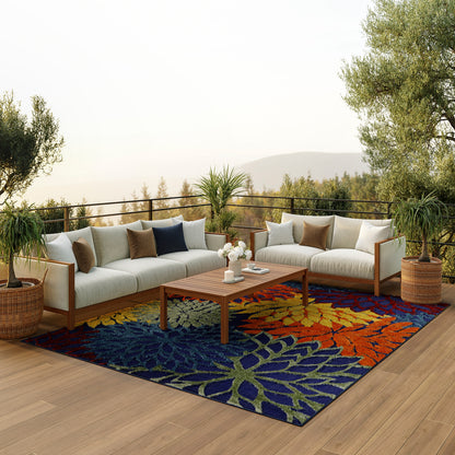 Outdoor sectional sofa with cream cushions on a vibrant multicolor leaf-pattern rug, wooden coffee table, and potted plants.