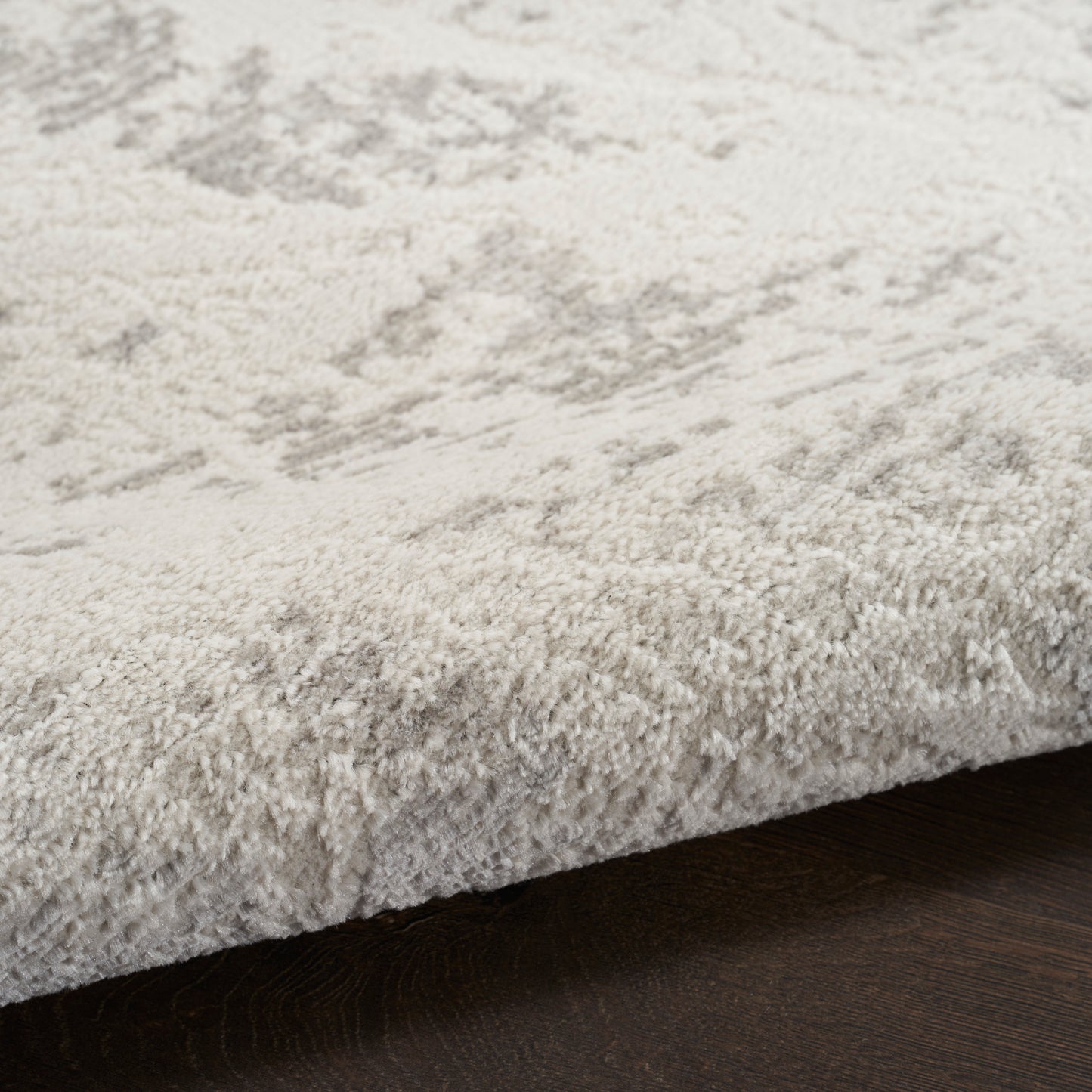 Cream plush area rug with subtle gray pattern, close-up edge resting on dark wooden floor
