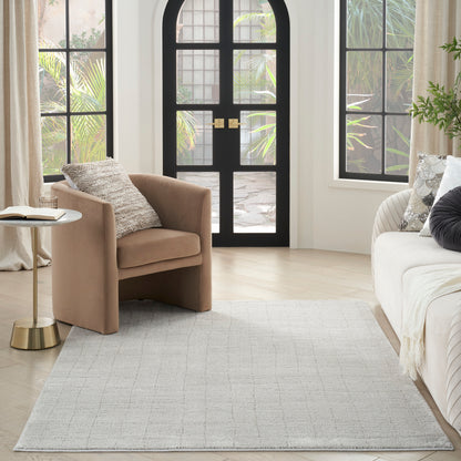Neutral Scandinavian 5' x 7' rug in a living room with tan upholstered chair & cream sofa, arched black glass door & brass round side table.
