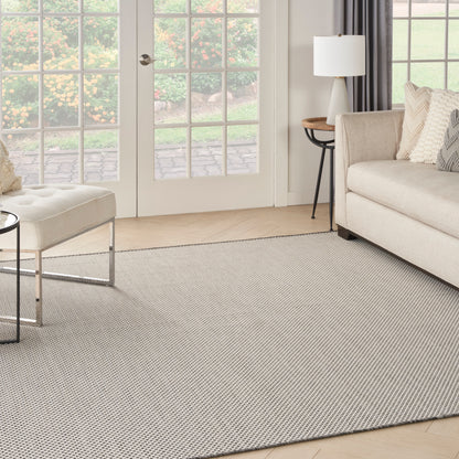 Neutral living room with beige sofa, matching ottoman, light textured rug, glass doors to garden, and side table lamp.