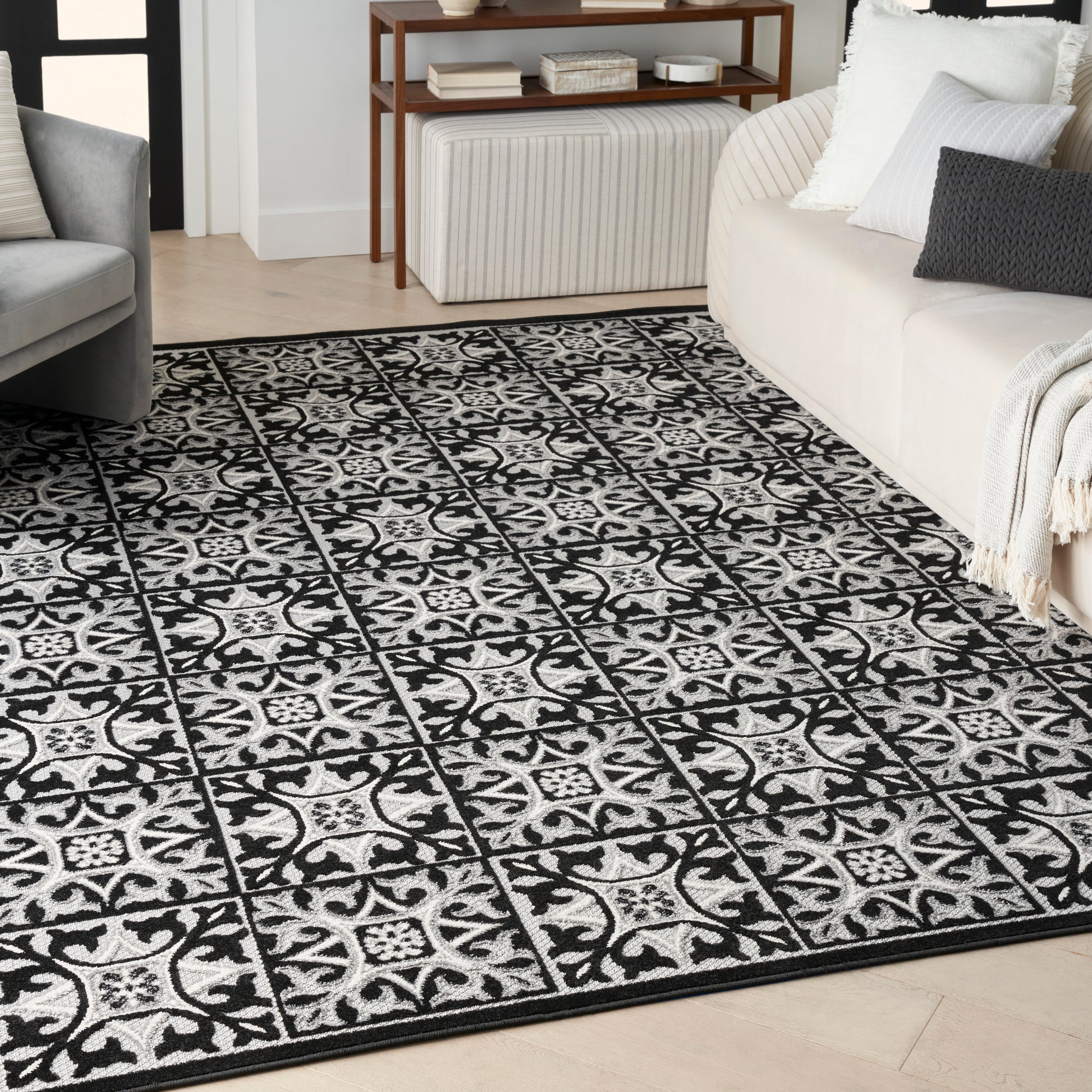 Black-and-white patterned area rug with square tile-like motifs on a light wood floor in a contemporary living room.