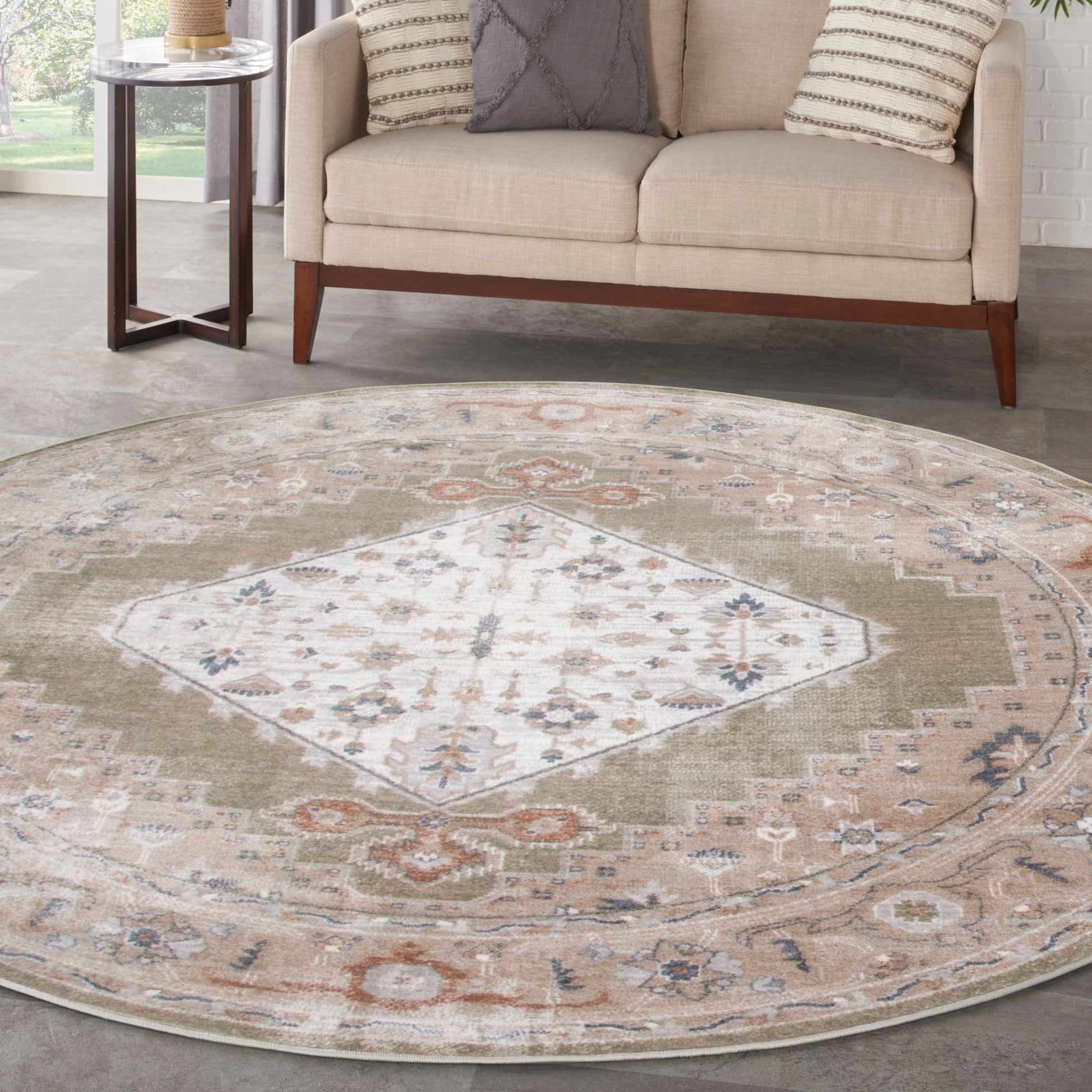 Round area rug with a faded ivory central diamond medallion and sage, tan, rust hues; complements beige sofa.