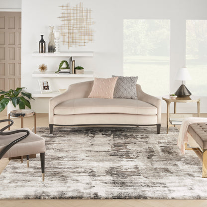 Gray rug in a bright living room with a beige fabric sofa and dark wood legs, peach and gray cushions, white shelves and plants.