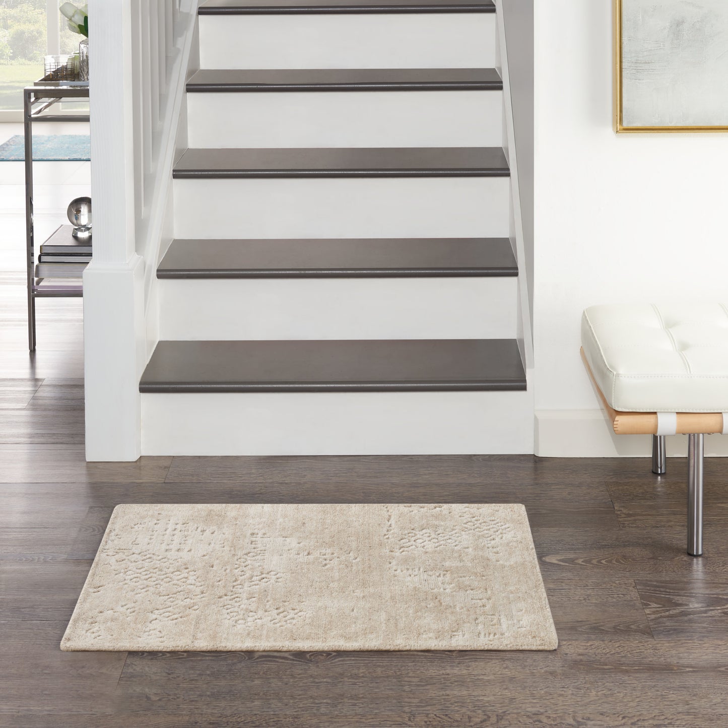 Beige textured rug on dark wood floor in a modern entryway with white staircase, dark gray treads, and a white padded bench.
