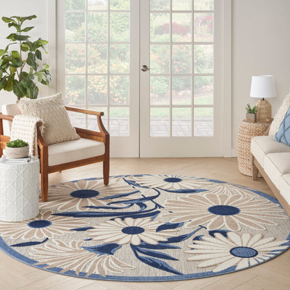 Round beige rug with large cream daisy motifs and navy blue accents in a sunlit living room by French doors.