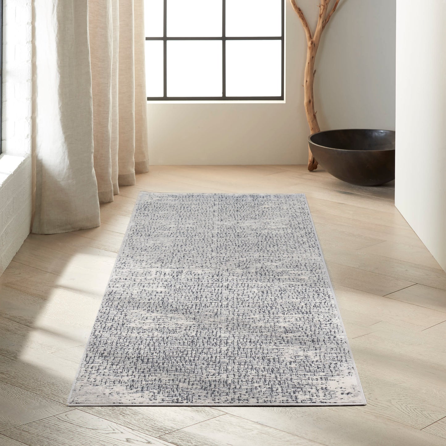 Blue-gray patterned runner rug on light wood floor in bright room with beige curtains.