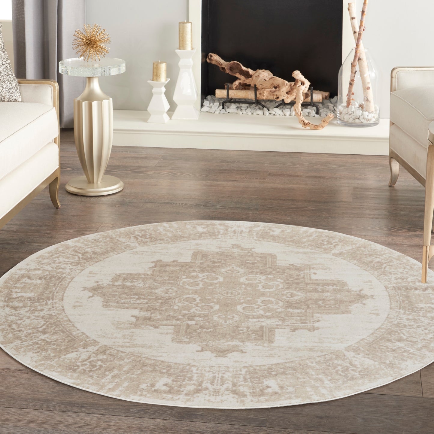 Round beige & ivory oriental-style rug on dark wood floor, complemented by cream sofas & a mantel fireplace scene.