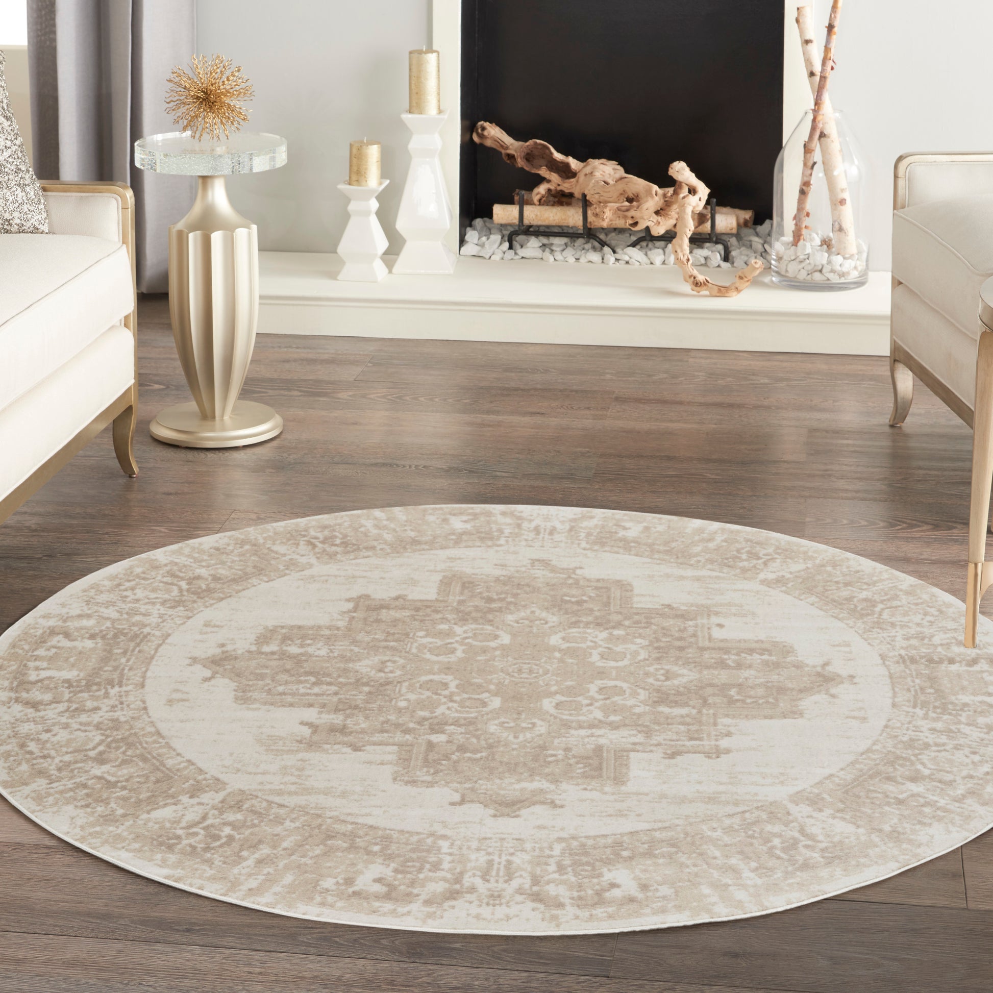 Round beige & ivory oriental-style rug on dark wood floor, complemented by cream sofas & a mantel fireplace scene.