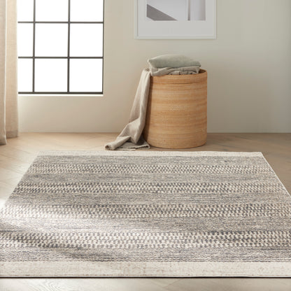 Neutral flatwoven rug with grey-beige stripes in a sunlit room, beside a round jute basket with folded throws.