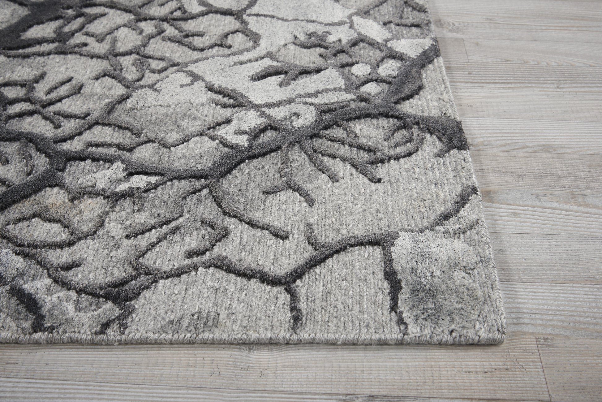 Gray and charcoal patterned area rug with branch-like motif on light wood floor.
