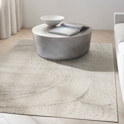 Grey cylindrical concrete coffee table with white round top, beige swirl-pattern rug, open magazine and white bowl in a modern living room.