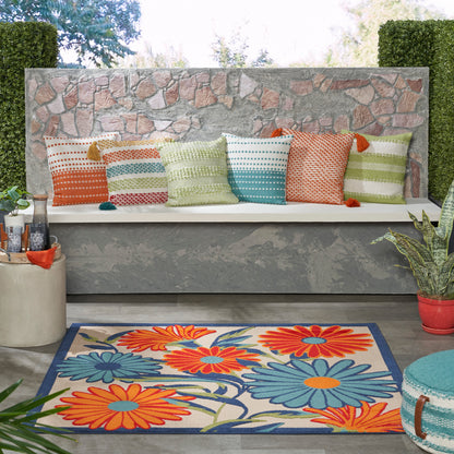 Outdoor lounge with stone wall bench and multicolor striped pillows; bright floral rug with orange and blue blooms.