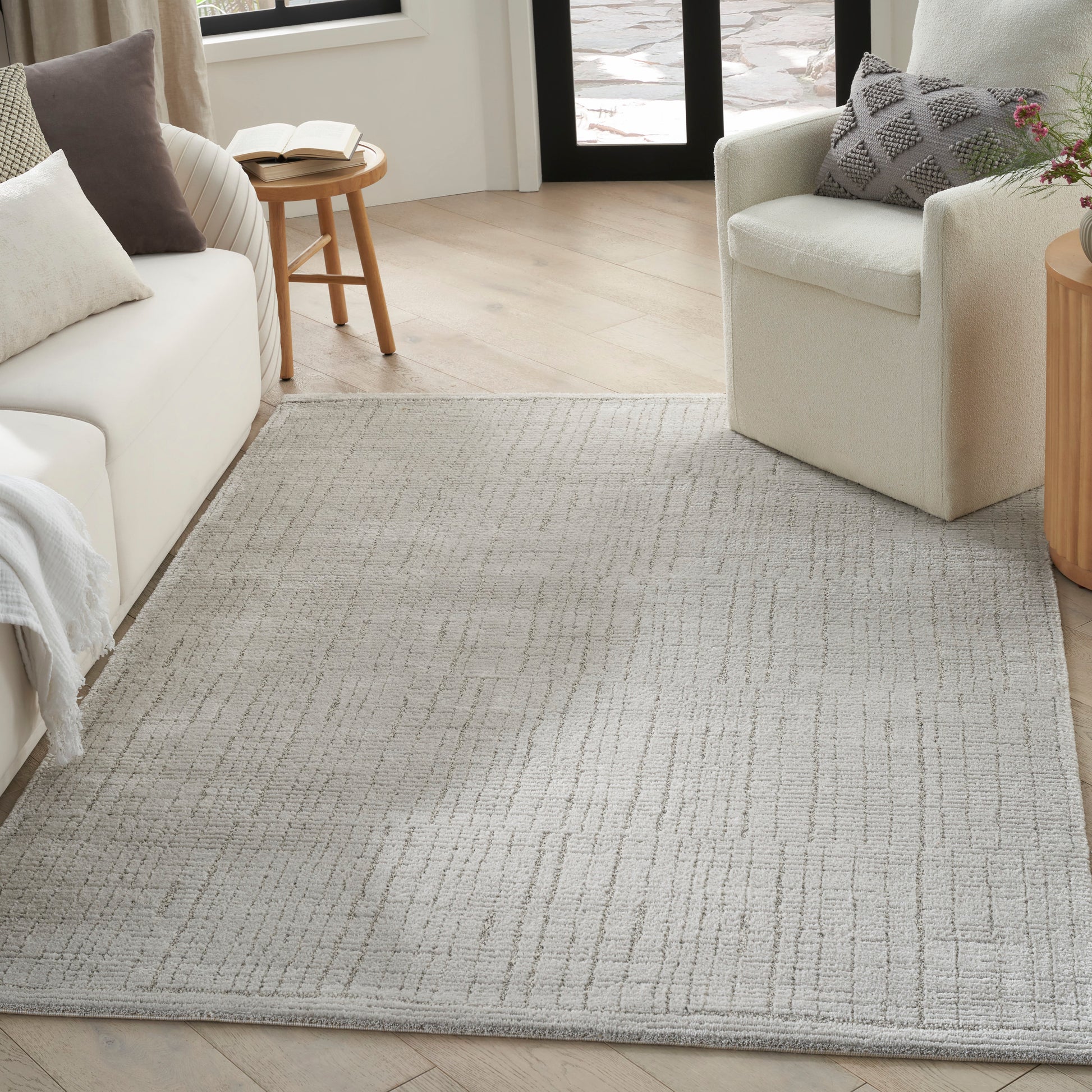 Soft, light gray area rug with subtle geometric border pattern in a cozy living room with a beige sofa and cream chair.