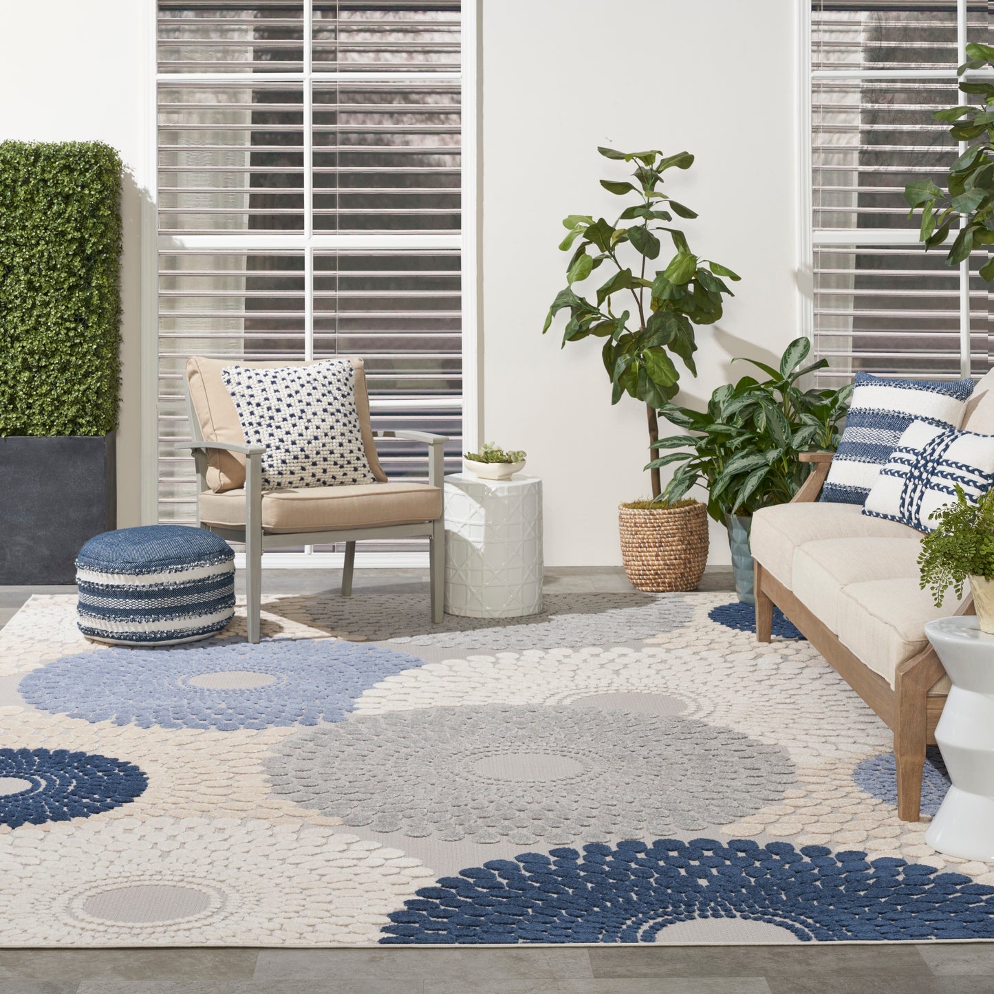 Bright living room featuring a rectangular blue-gray rug, beige sofa and armchair, blue and white cushions, and potted plants.