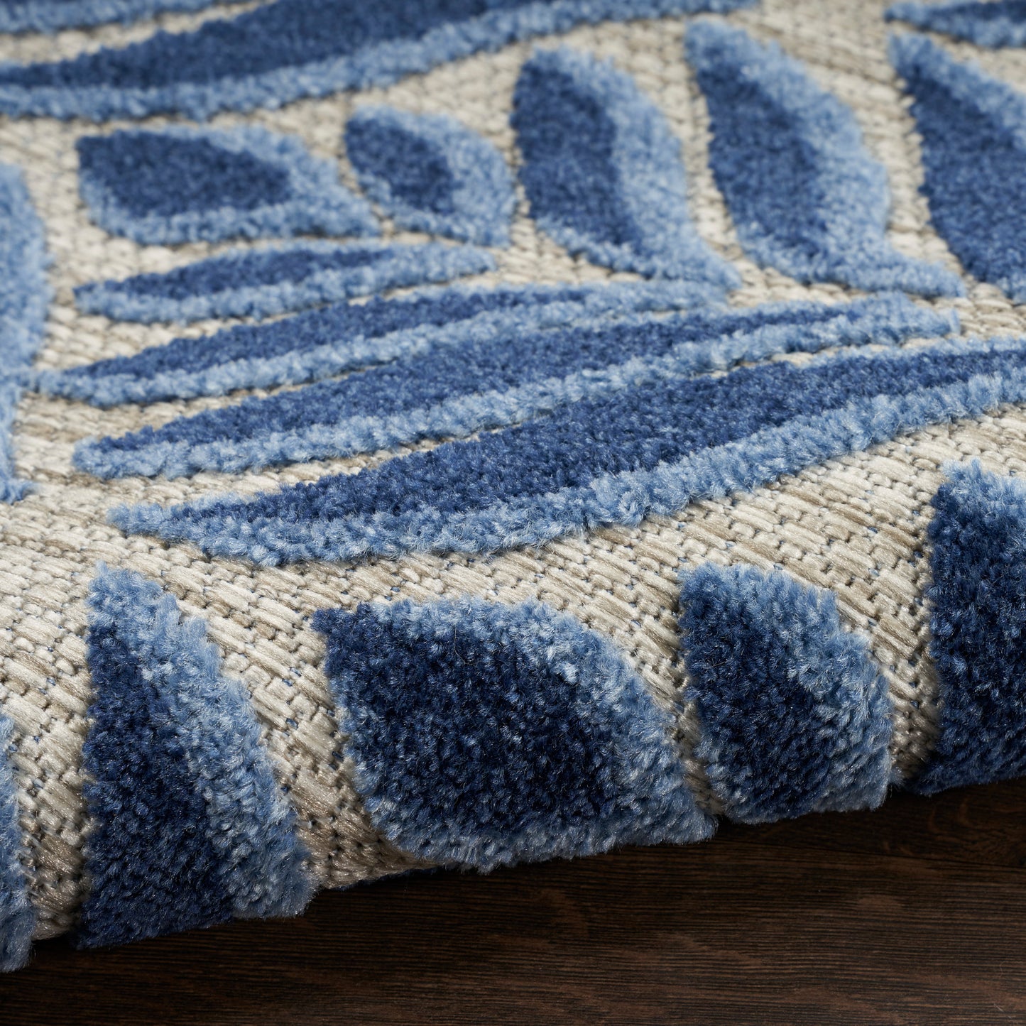 Close-up of a blue and beige shag rug with raised geometric patterns on a woven base; plush navy and light-blue pile.