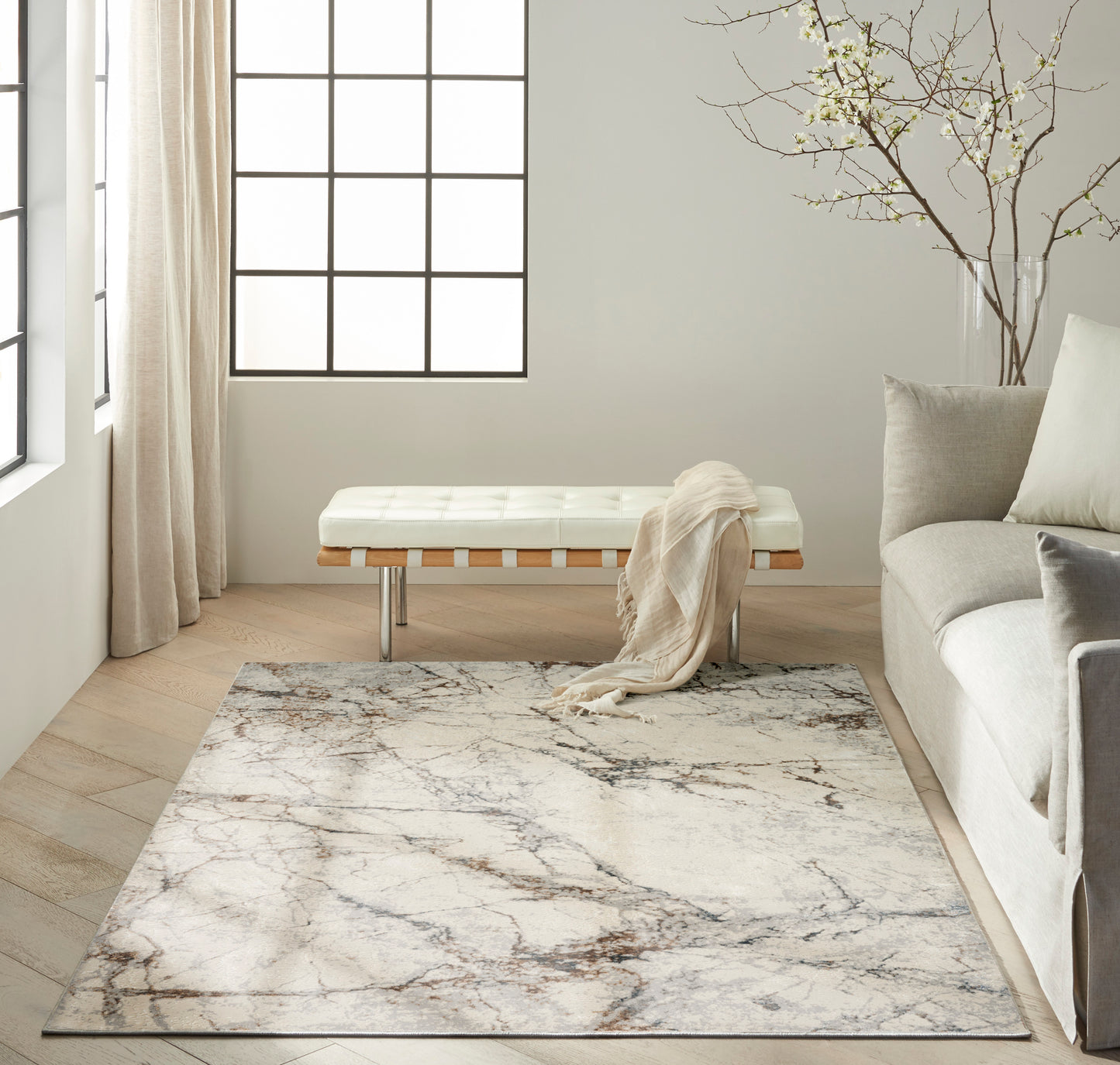 Modern neutral living room with ivory tufted bench, wood slats and metal legs, marble-pattern rug, beige sofa & throw.