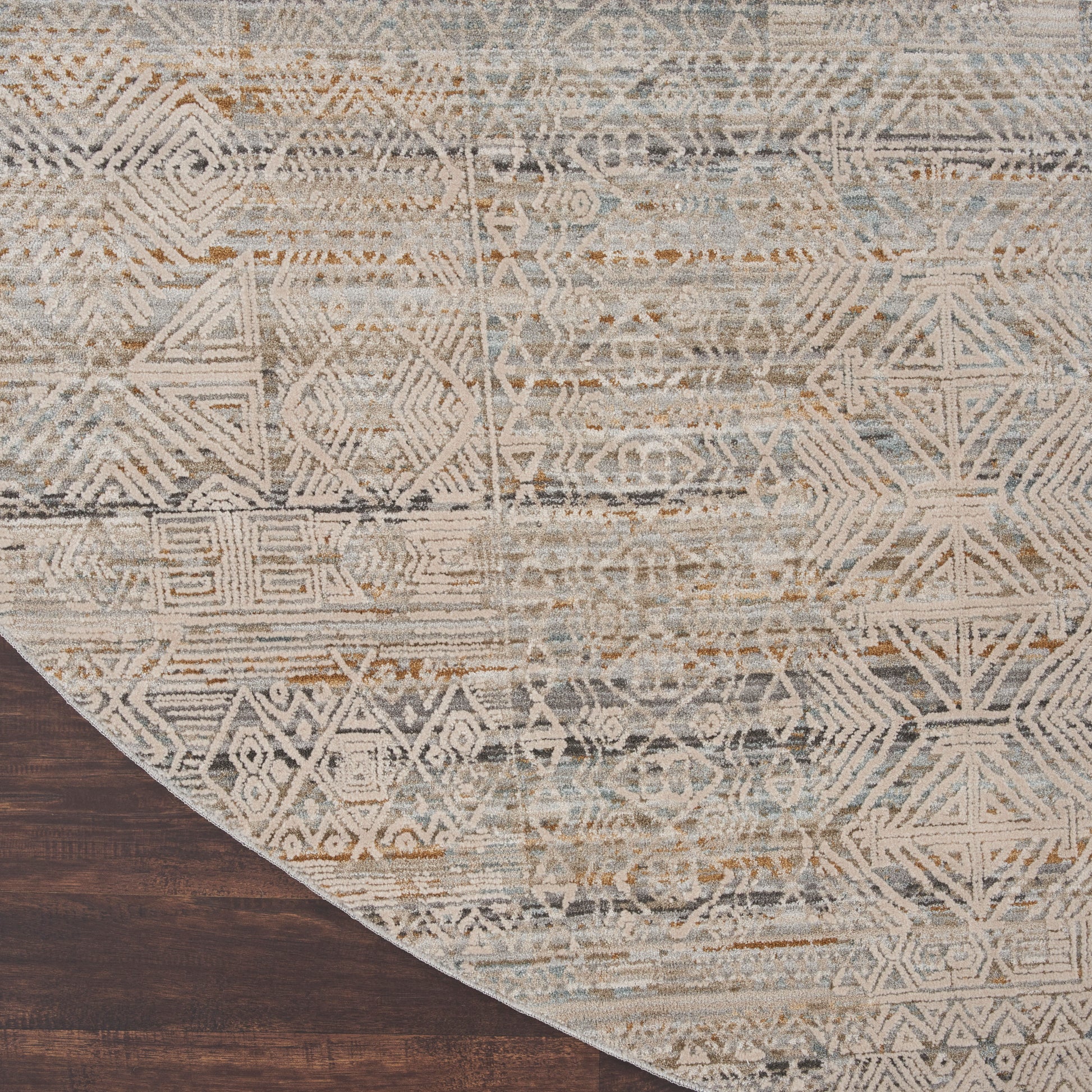 Round area rug with distressed geometric motifs in ivory, blue & tan on dark wood floor.