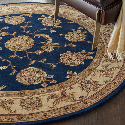 Circular oriental rug: deep blue center with gold floral vines and border; beside a leather chair with a fringed throw.