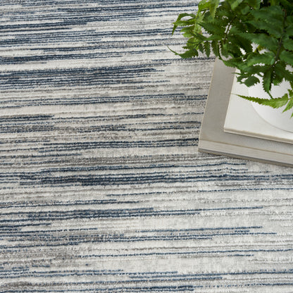 Blue-gray striped rug with irregular horizontal lines beside a potted fern on a light stack of books.