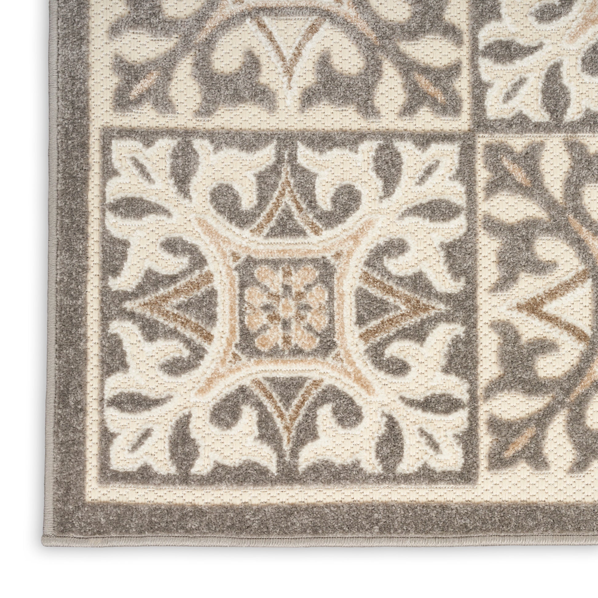 Beige and gray ornate rug corner with tile-like blocks, scrolling floral motif, and thick border.