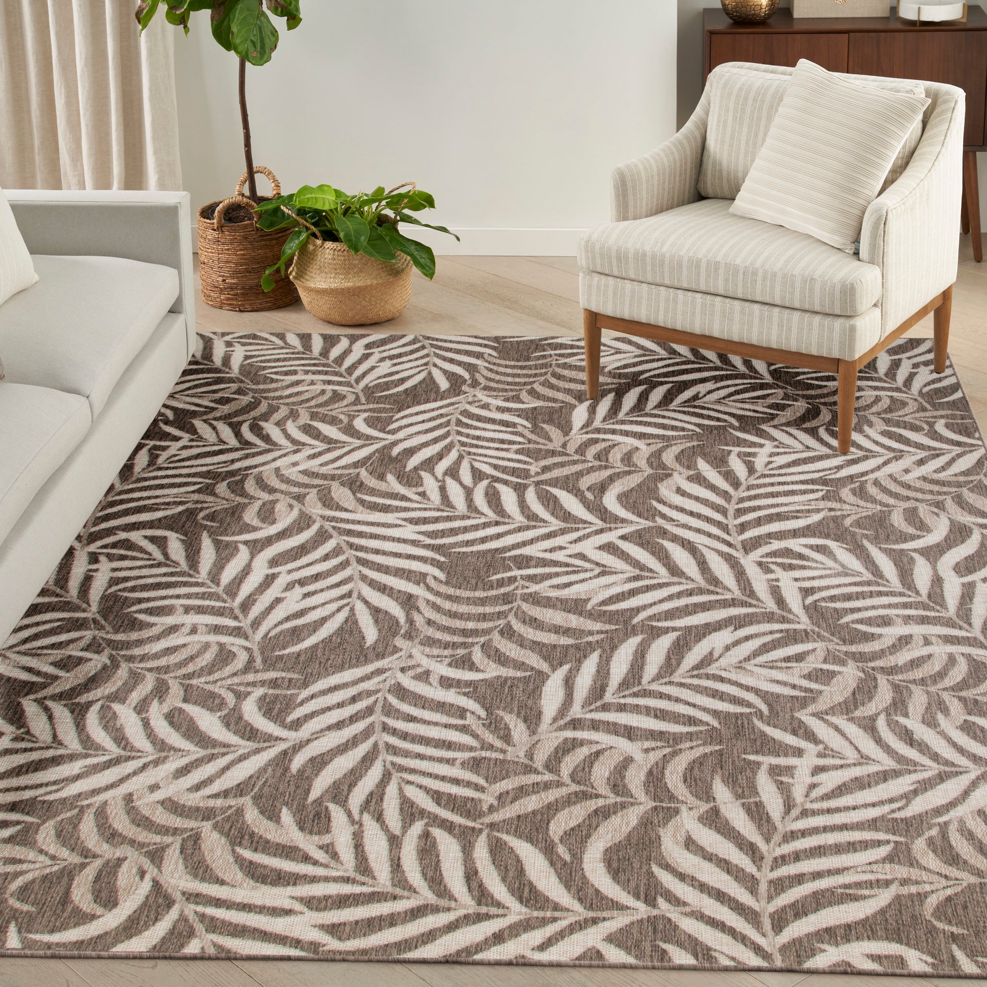 Cream striped armchair with wooden legs on a brown & ivory palm-leaf patterned rug; potted plants nearby.