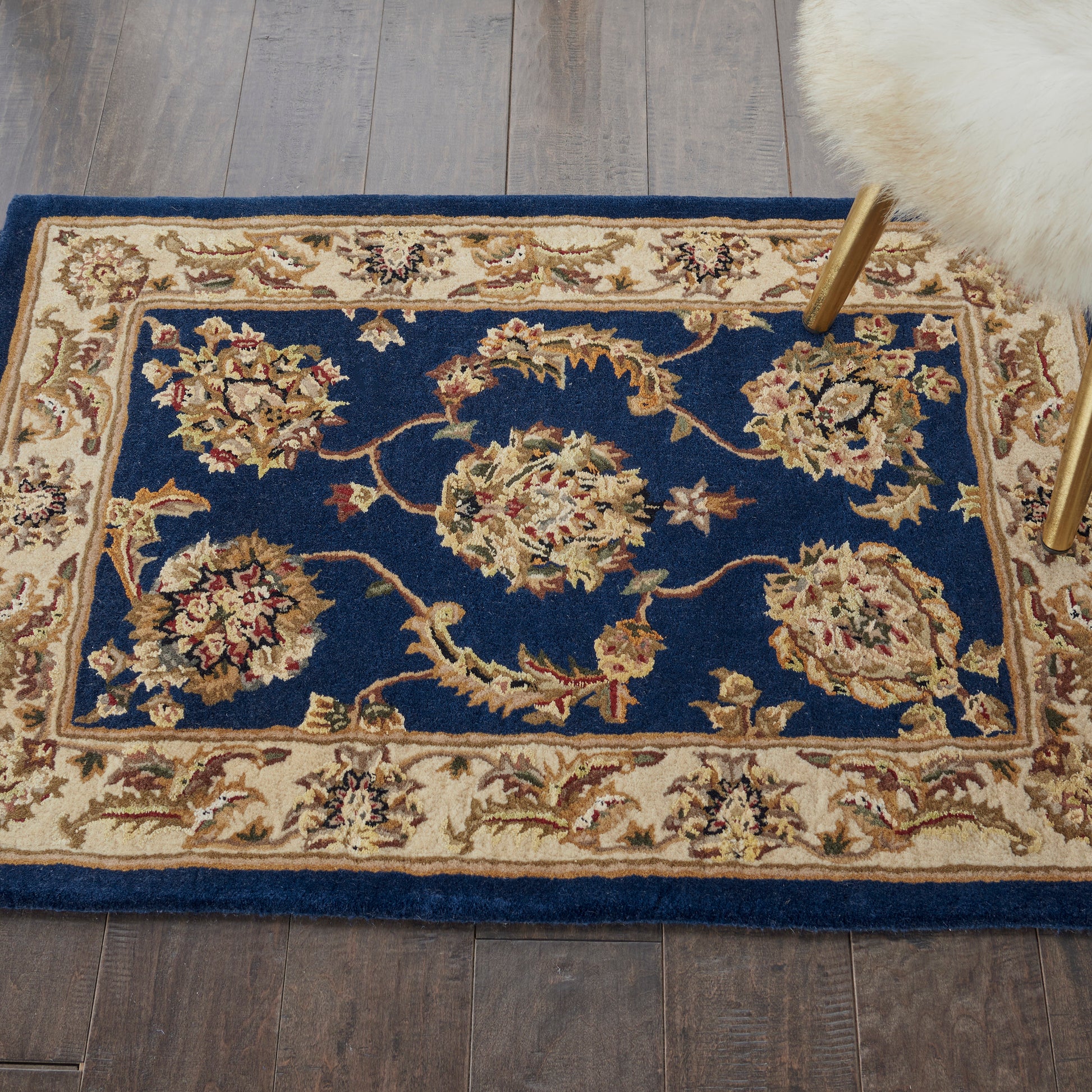 Persian-style area rug with deep blue field, cream-gold floral medallions, and ivory border on wooden floor.