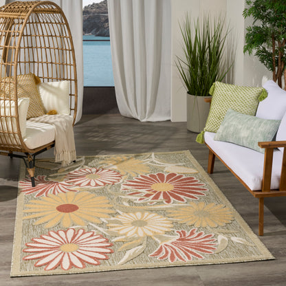 Coastal outdoor scene with wicker egg chair, beige floral outdoor rug with large daisies (5' x 8'), white sofa and green cushions.