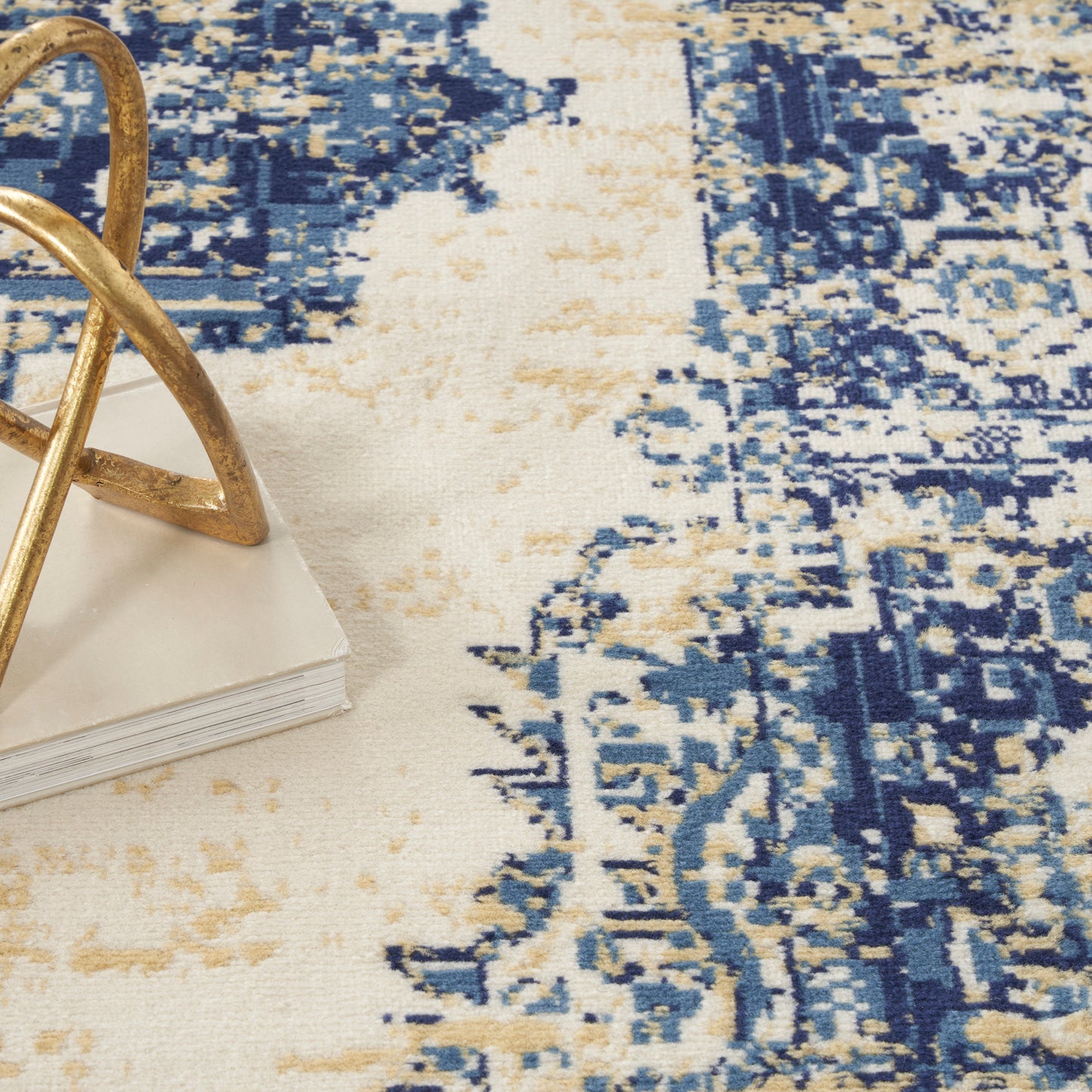 Blue and beige distressed area rug with cream accents, plus a gold-tone geometric metal ornament on a white book.