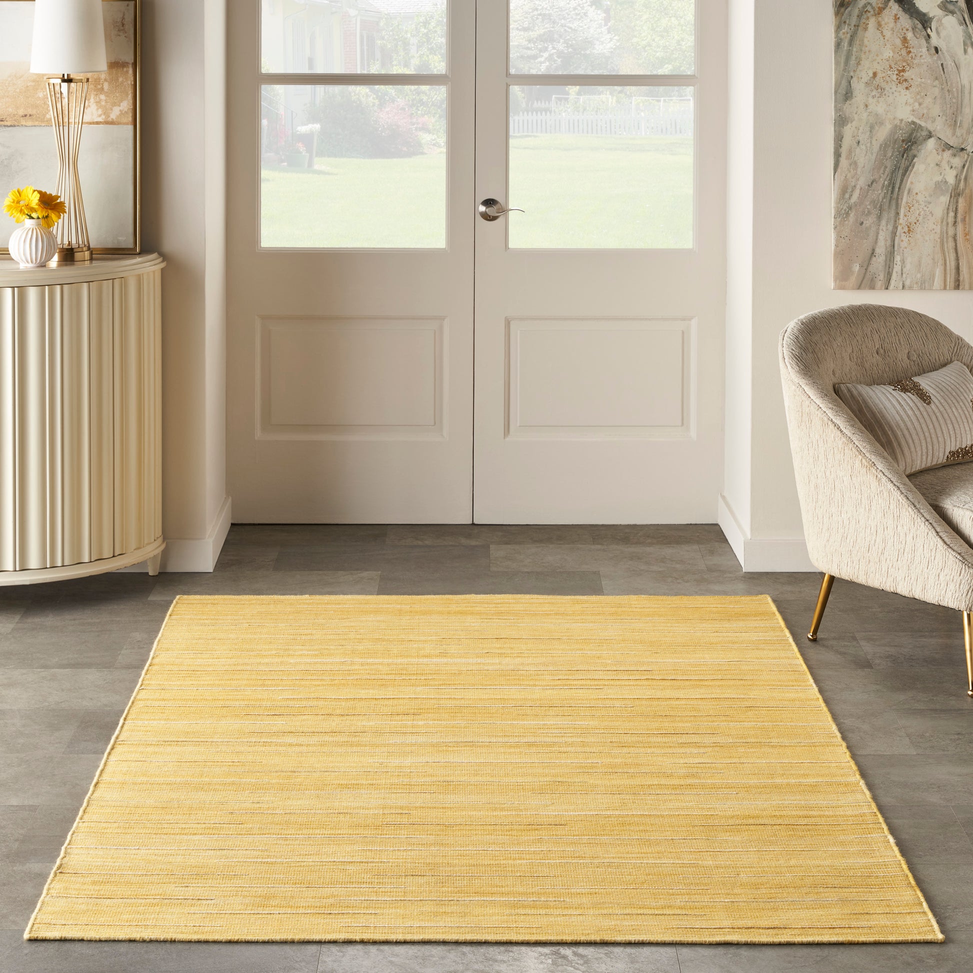 Yellow rectangular woven rug in entryway with white double doors, beige curved sofa and sunflowers on a sideboard.