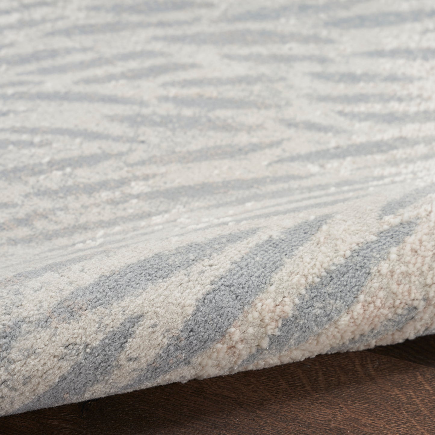 Blue and beige zigzag rug with textured pile, folded edge on dark wood floor.