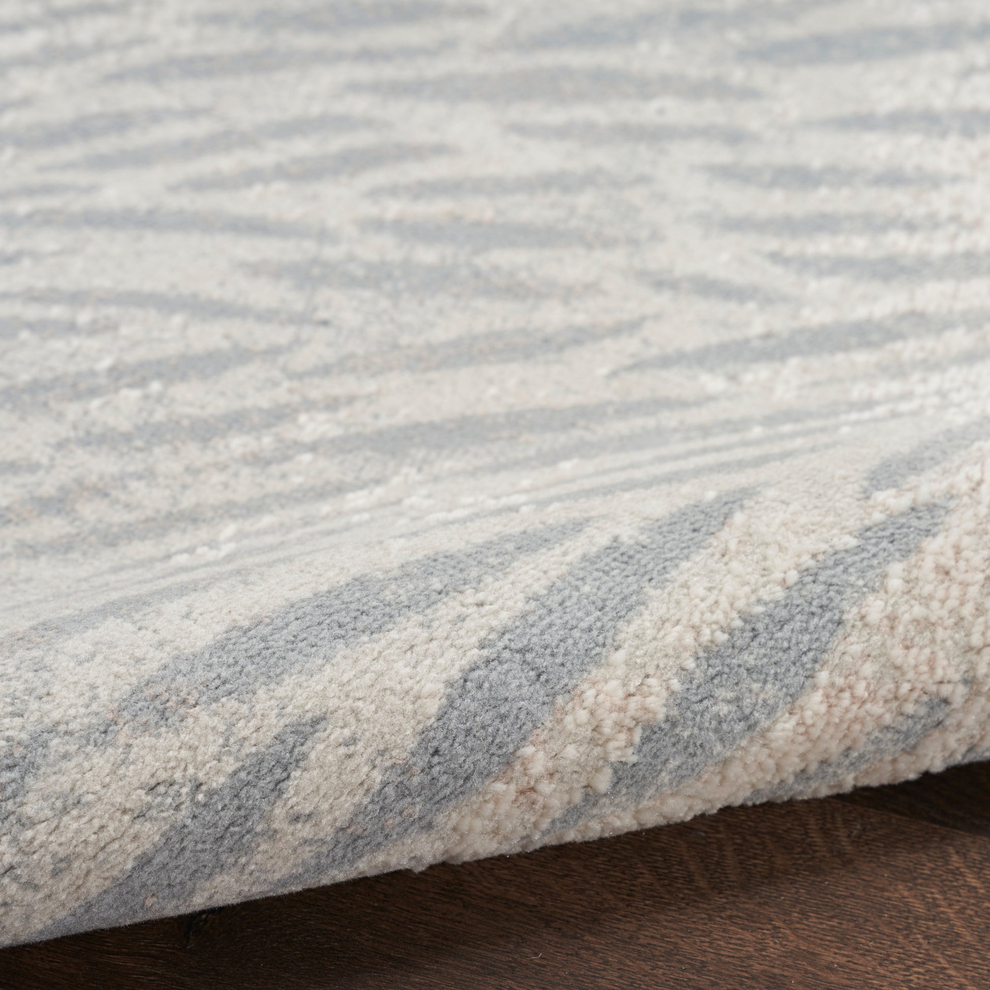 Blue and beige zigzag rug with textured pile, folded edge on dark wood floor.
