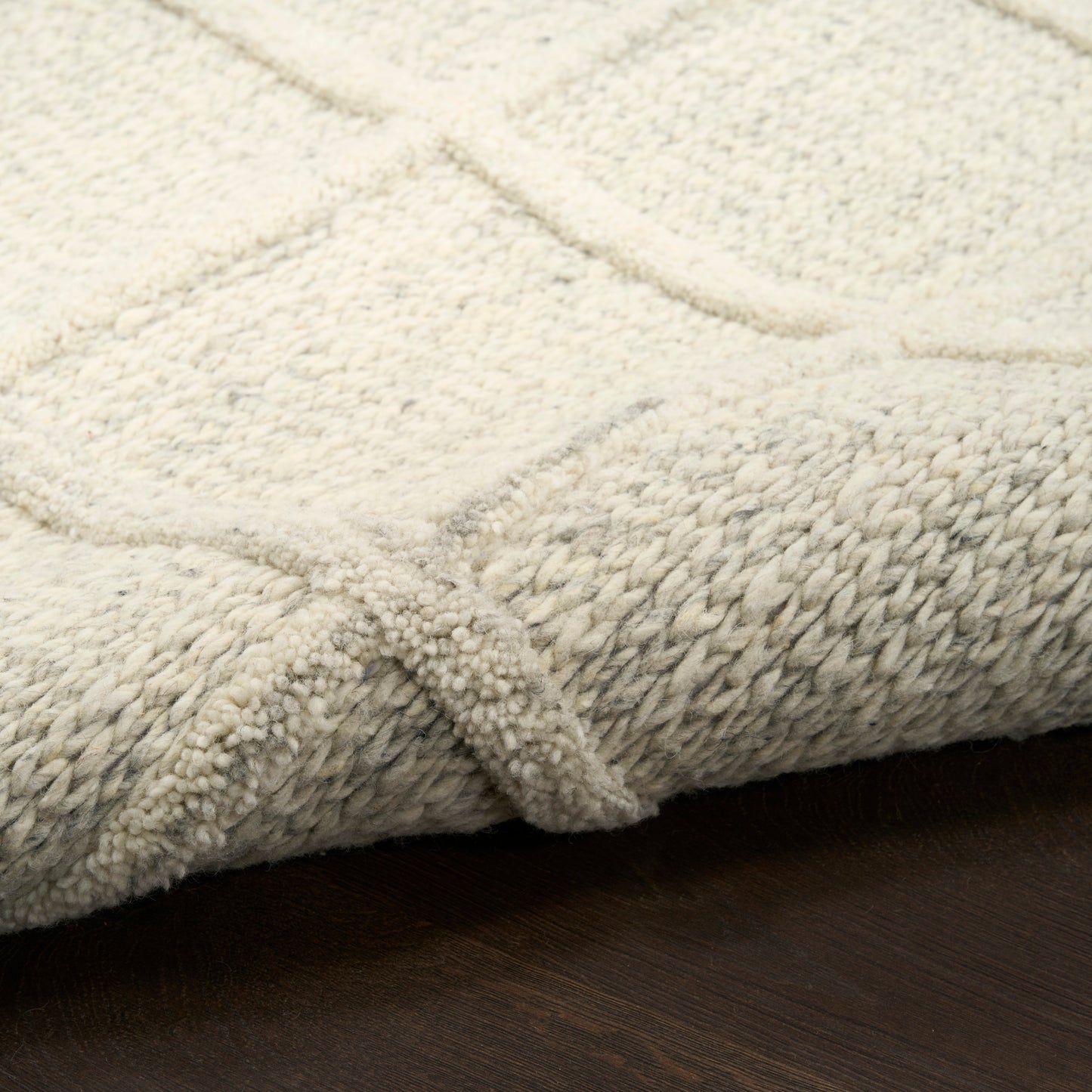 Cream beige textured rug with geometric lines and thick looping pile, folded edge on dark wooden floor.