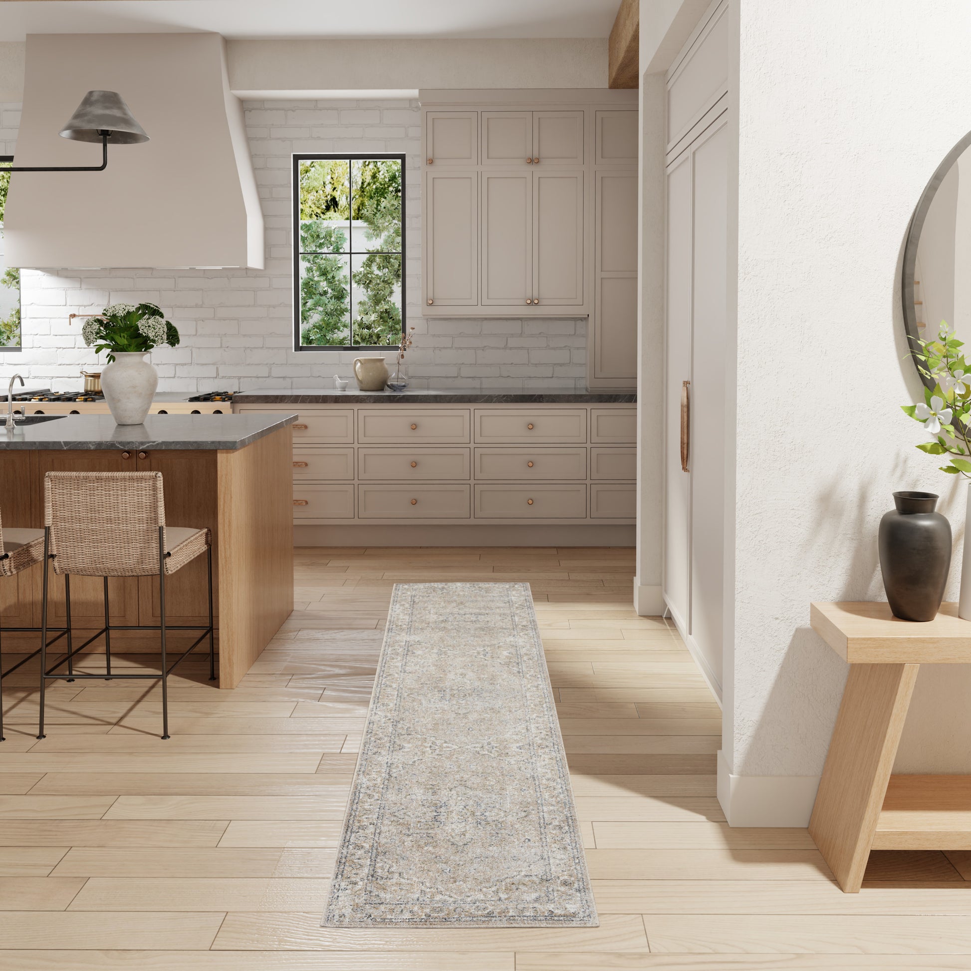 Bright kitchen with cream cabinets, gray countertops, wooden island, woven stools, light patterned runner rug and greenery.