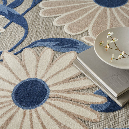 Beige and blue floral rug with large daisy motifs, beside stacked gray books and a white ceramic bowl with blossoms.
