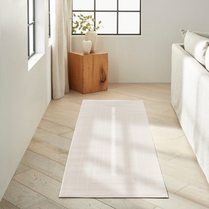 Cream-toned runner rug with subtle chevron pattern on light wood floor beside a pale sofa in a bright minimal living room.