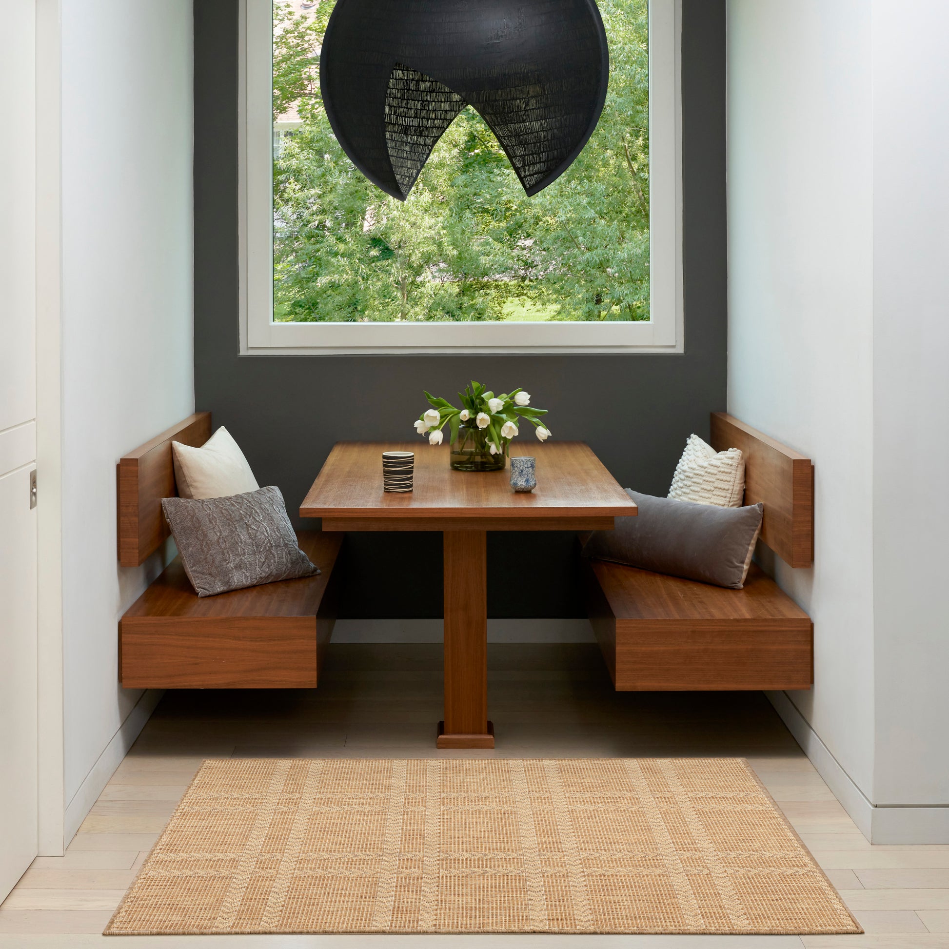 Modern 3' x 5' rug in gray and beige tones in a booth-style dining nook with a square table, timber benches, gray and beige cushions, a black pendant lamp, and a window view.
