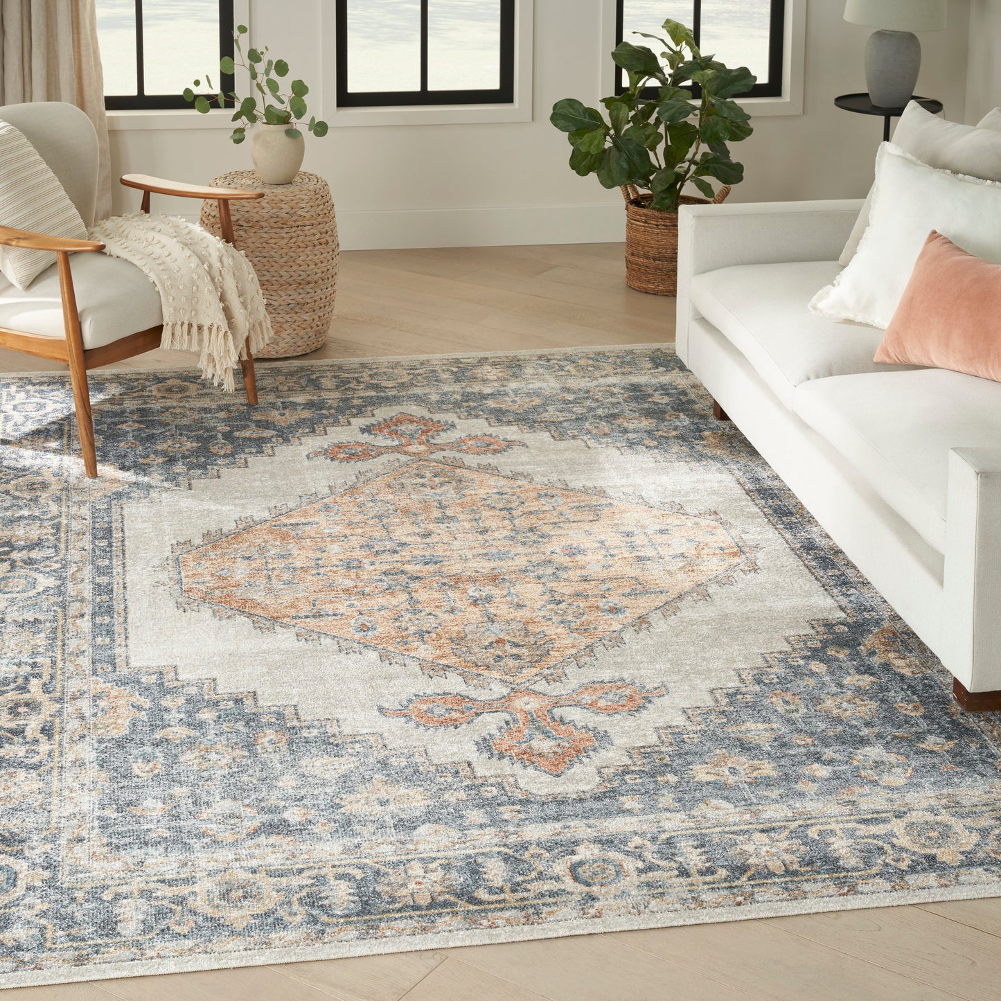Bright living room featuring a large blue and ivory oriental rug, white sofa, light wood armchair, and potted plants.