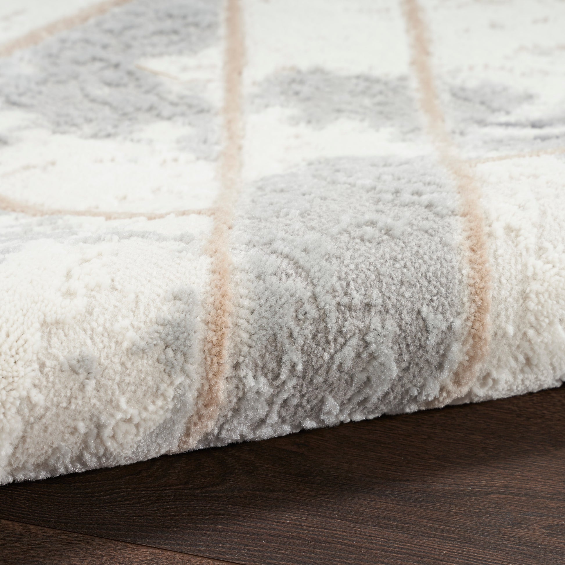 Close-up of a plush cream-gray area rug with tan stripes resting on dark wood floor.