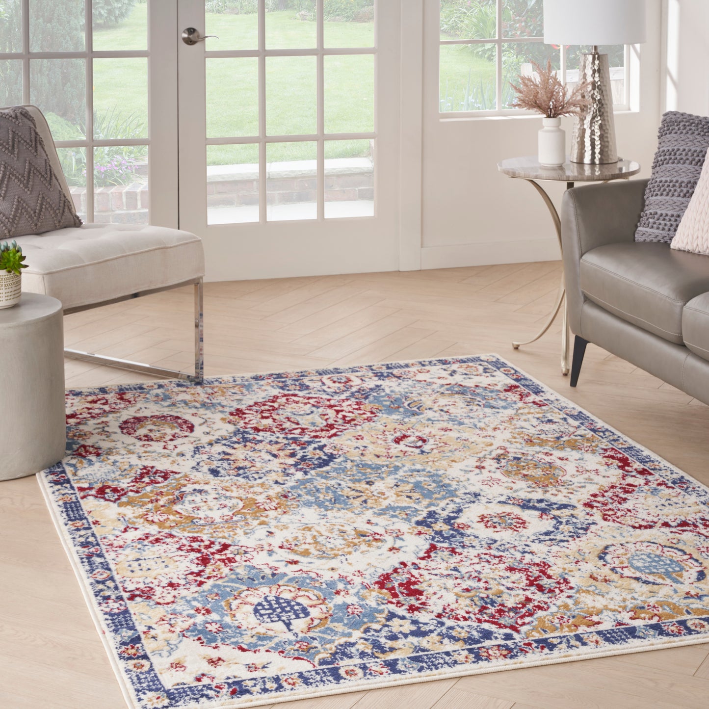 Traditional area rug with red, blue and ivory floral medallions on light wood floor in a bright living room with beige sofa.