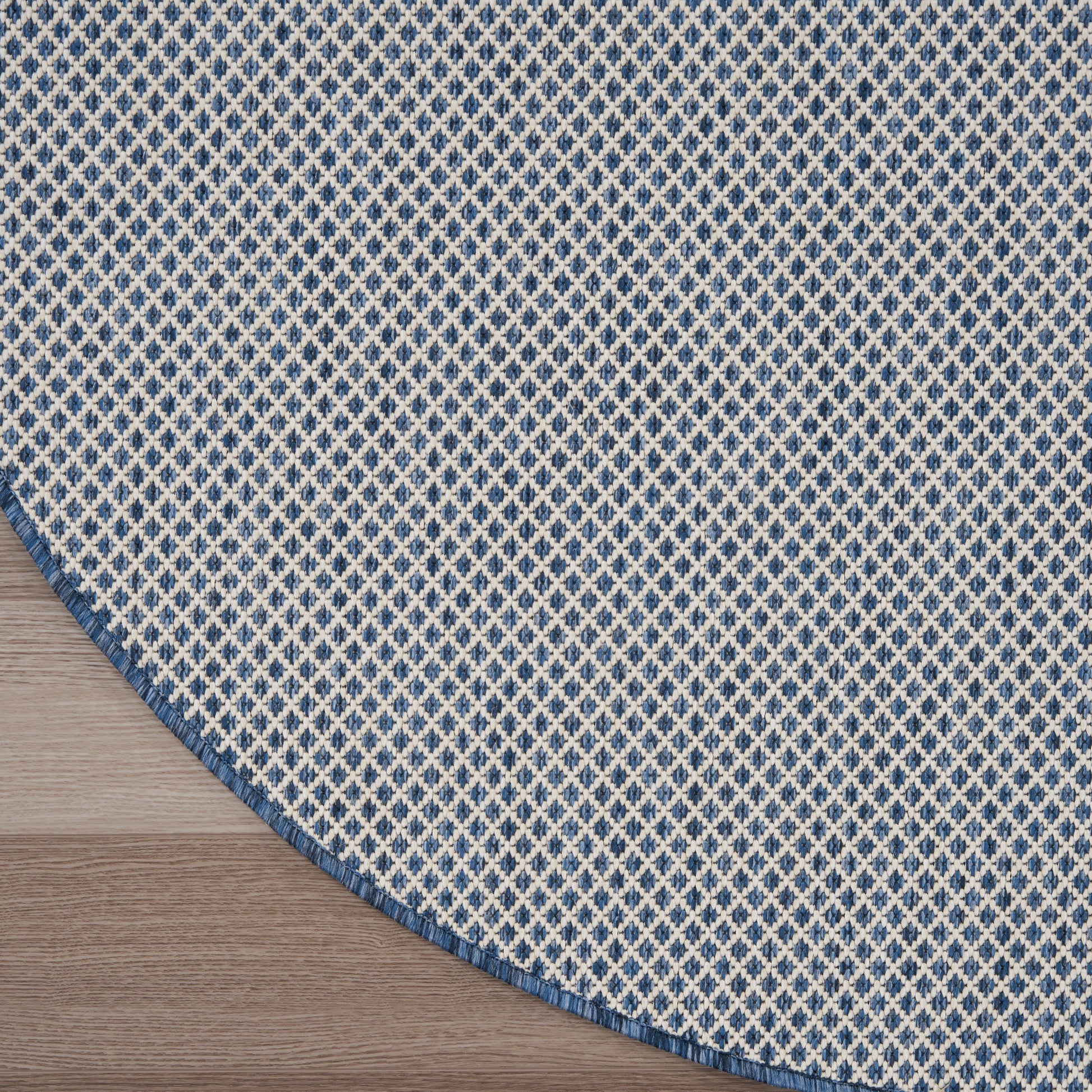 Blue and white diamond patterned round rug on a light wood table against a gray background.