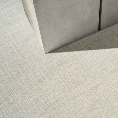 Beige textured rug with subtle linear pattern; leaning gray concrete blocks create minimalist modern decor.