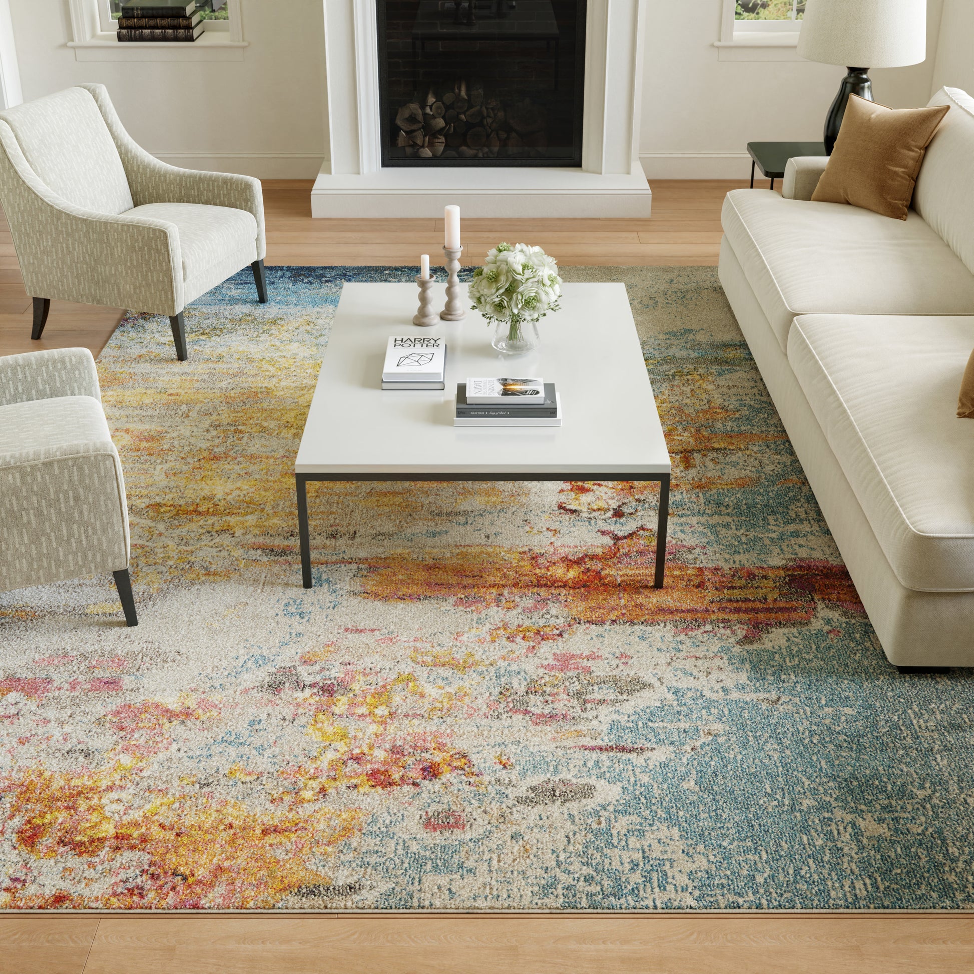 Modern living room with cream sofa and armchairs, white square coffee table, colorful abstract rug, fireplace and decor.