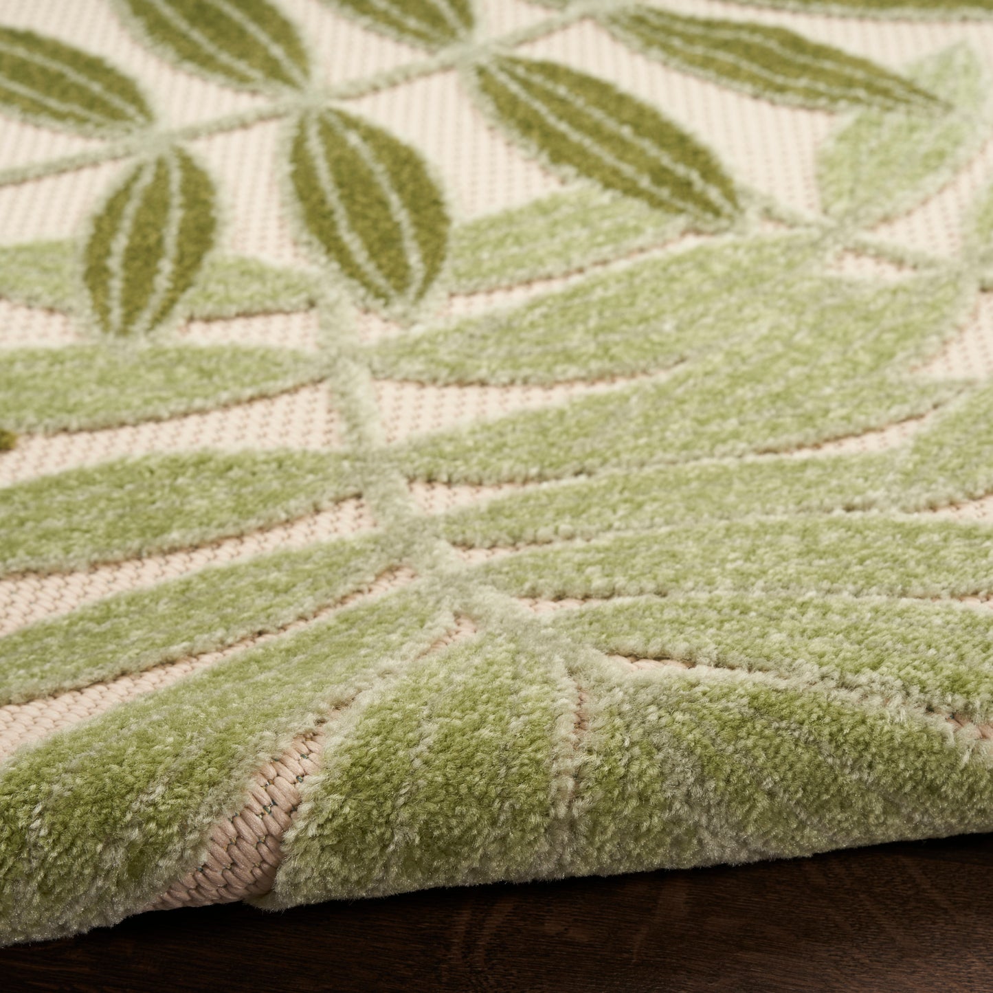 Close-up of a sage green botanical rug with raised leaf pattern on beige background; soft tufted texture.