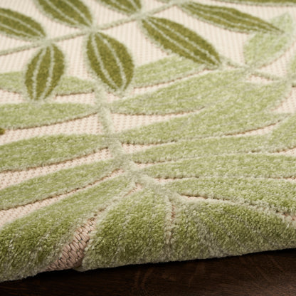 Close-up of a sage green botanical rug with raised leaf pattern on beige background; soft tufted texture.
