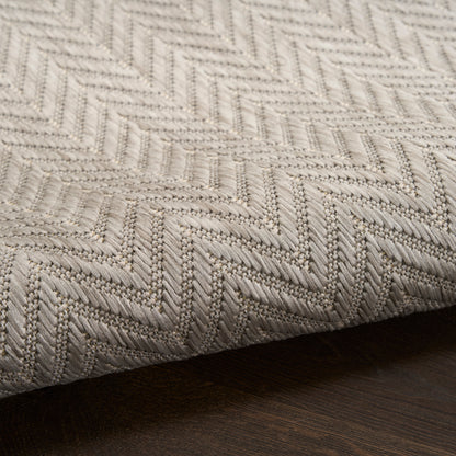 Beige chevron-patterned area rug with raised weave on dark wooden floor.